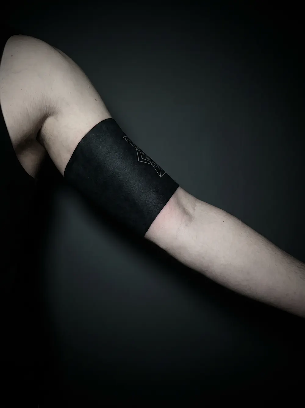 A solid blackout band wrapping an upper arm with a fine geometric motif in negative space — the densest way to cover old ink.
