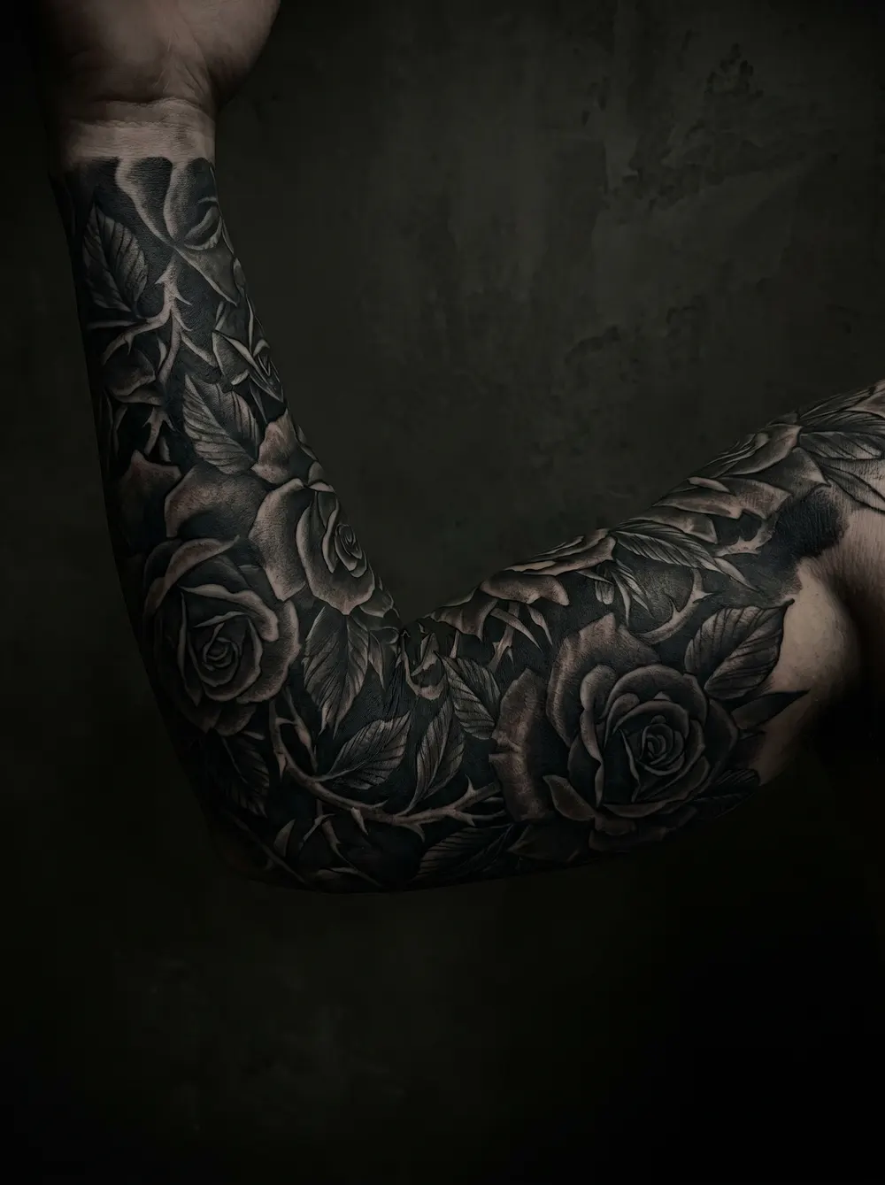 A dense black-and-grey rose cover-up wrapping the whole arm from upper arm to forearm, heavy shading and deep negative space between the blooms — the kind of saturated piece whose aftercare matters most.