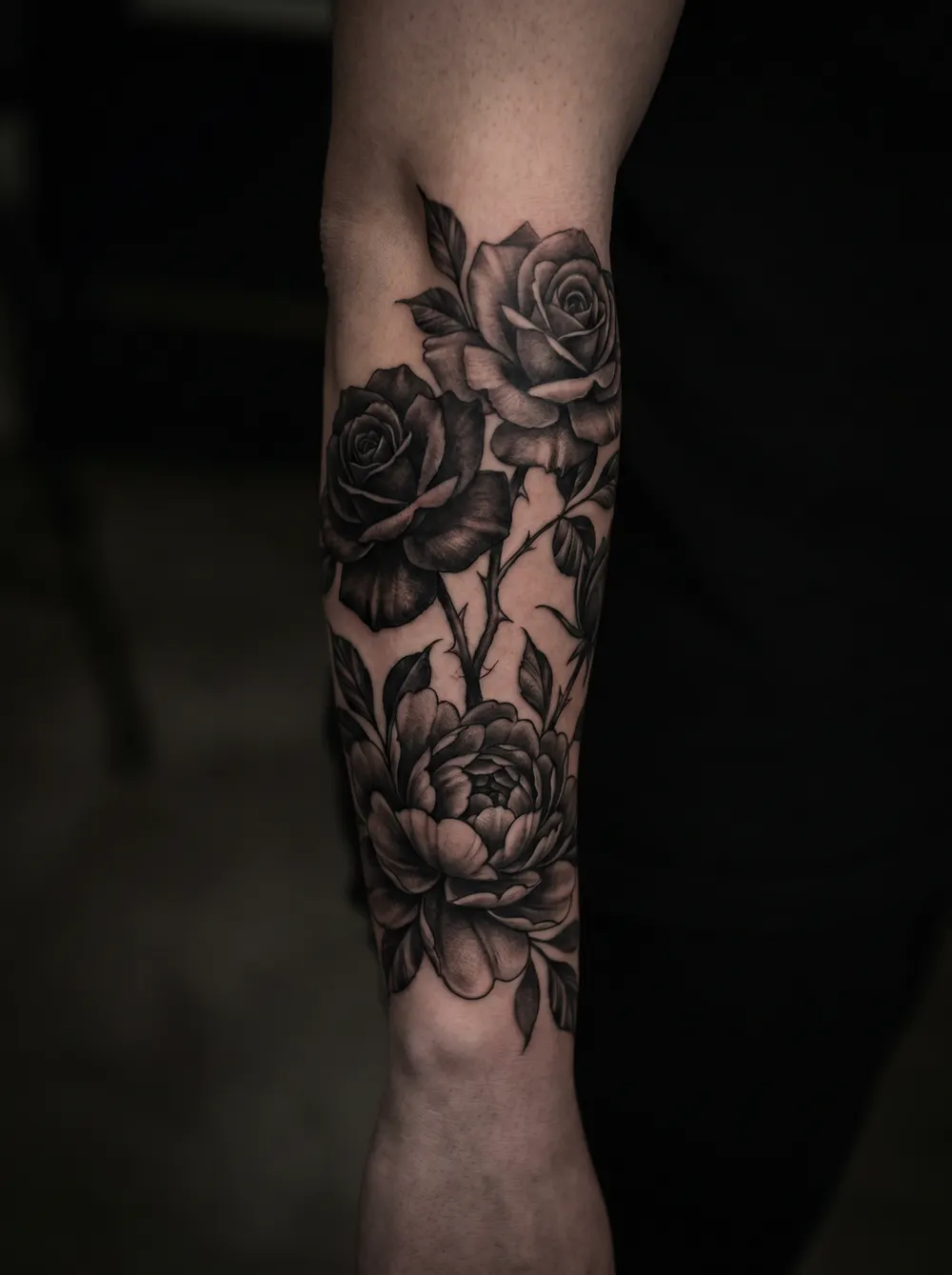 A black-and-grey rose and peony piece running down a forearm.